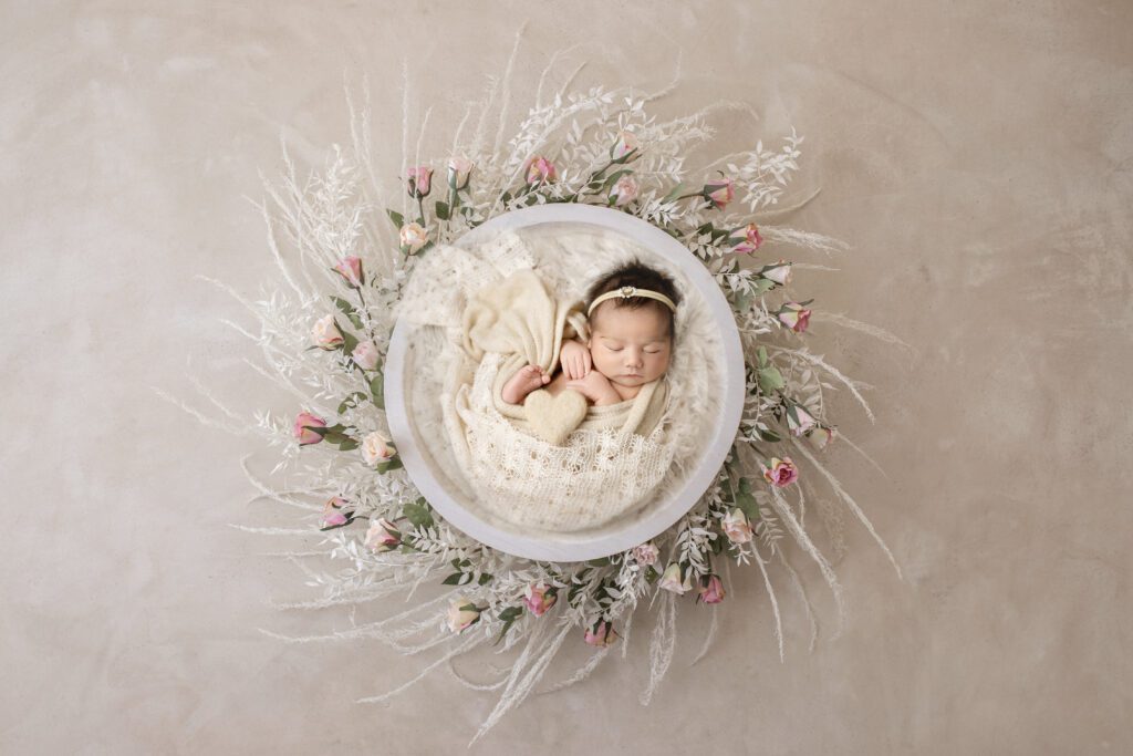 Newborn Baby girl wrapped inside a bowl with florals. Neutral tones and pink flowers. Wrapped in light yellow and white.