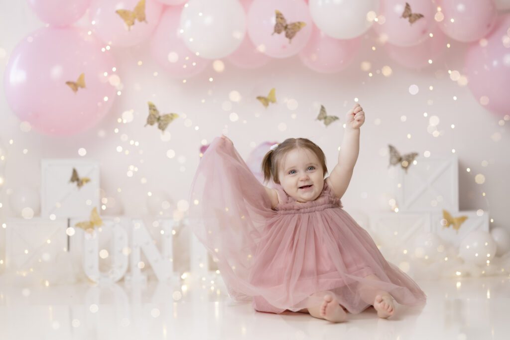 young girl in a pink tulle dress sitting in front of pink and white butterfly decor for her cake smash session edmonton