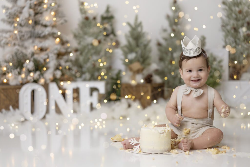 Little boy in tan overalls celebrating his first birthday with a christmas themed cake smash session edmonton