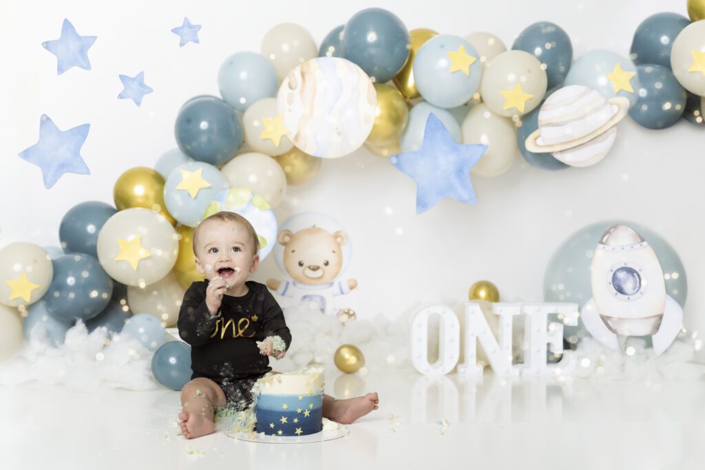 little boy in a black onesie surrounded by blue and gold space theme for his cake smash session edmonton