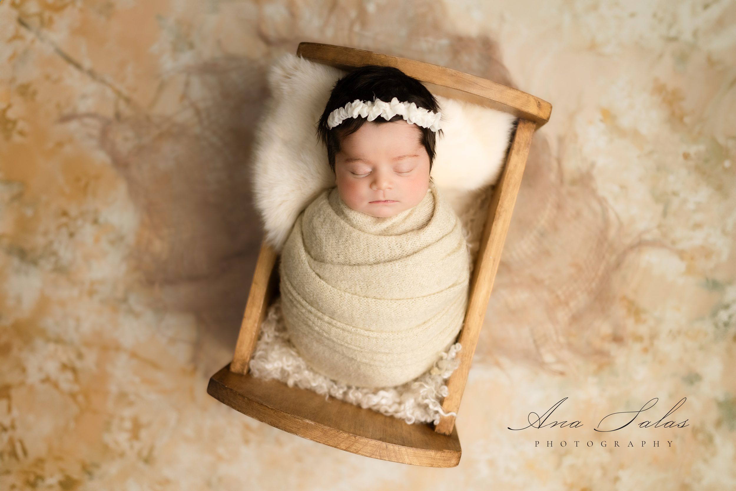 A newborn baby sleeps in a wooden crib in a studio while wrapped in a knit swaddle after using edmonton diaper service