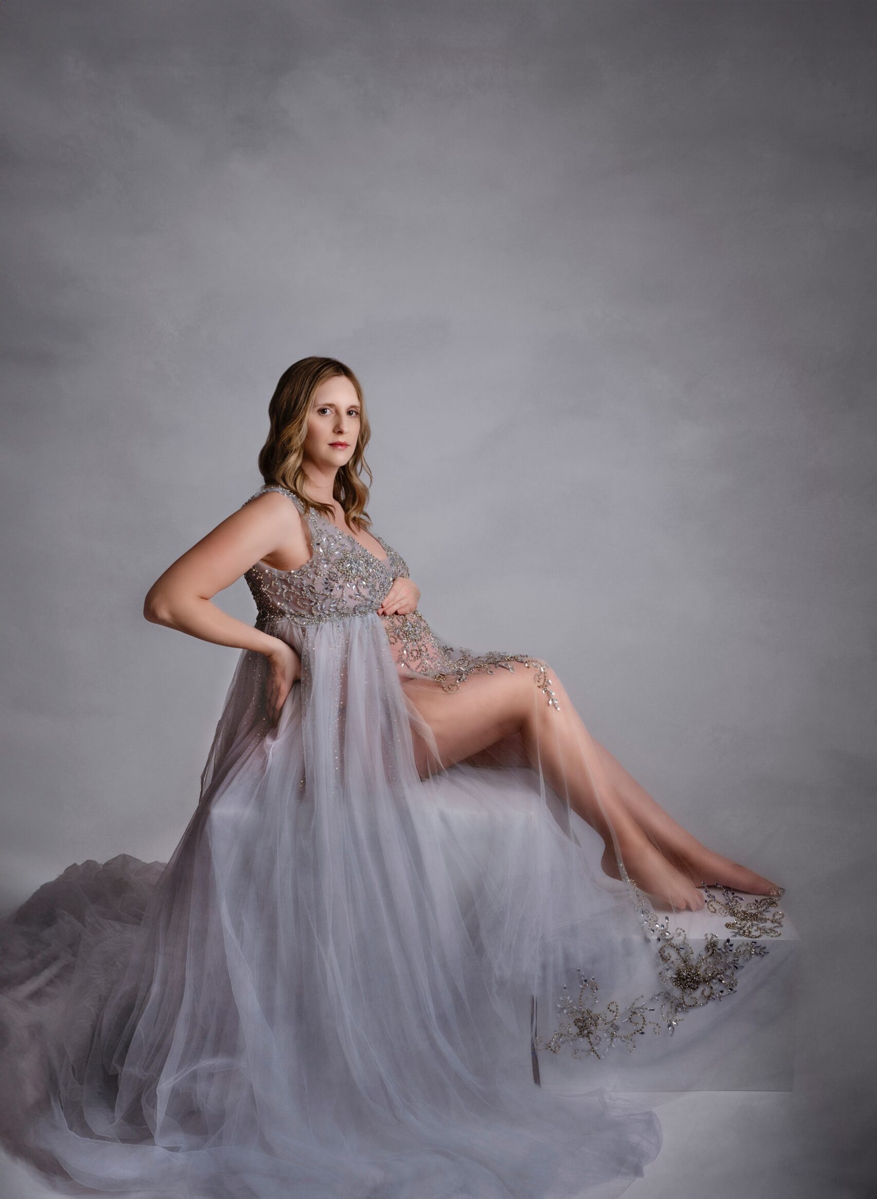 A mom to be sits in a flowing maternity gown in a studio before meeting edmonton midwives