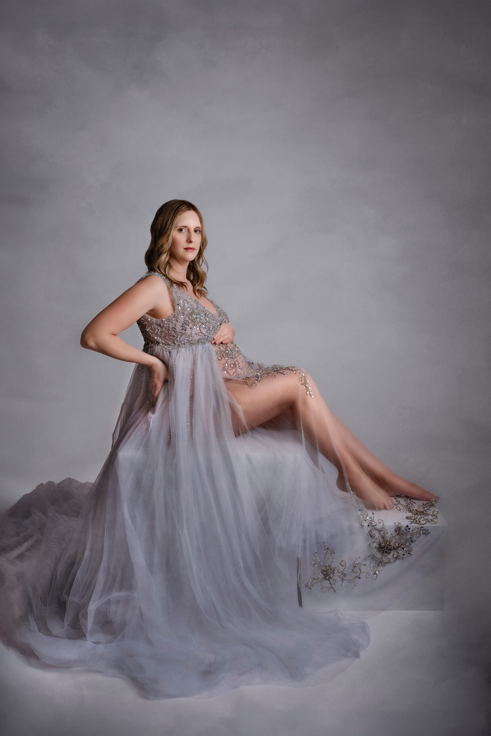 A mom to be sits in a flowing maternity gown in a studio before meeting edmonton midwives