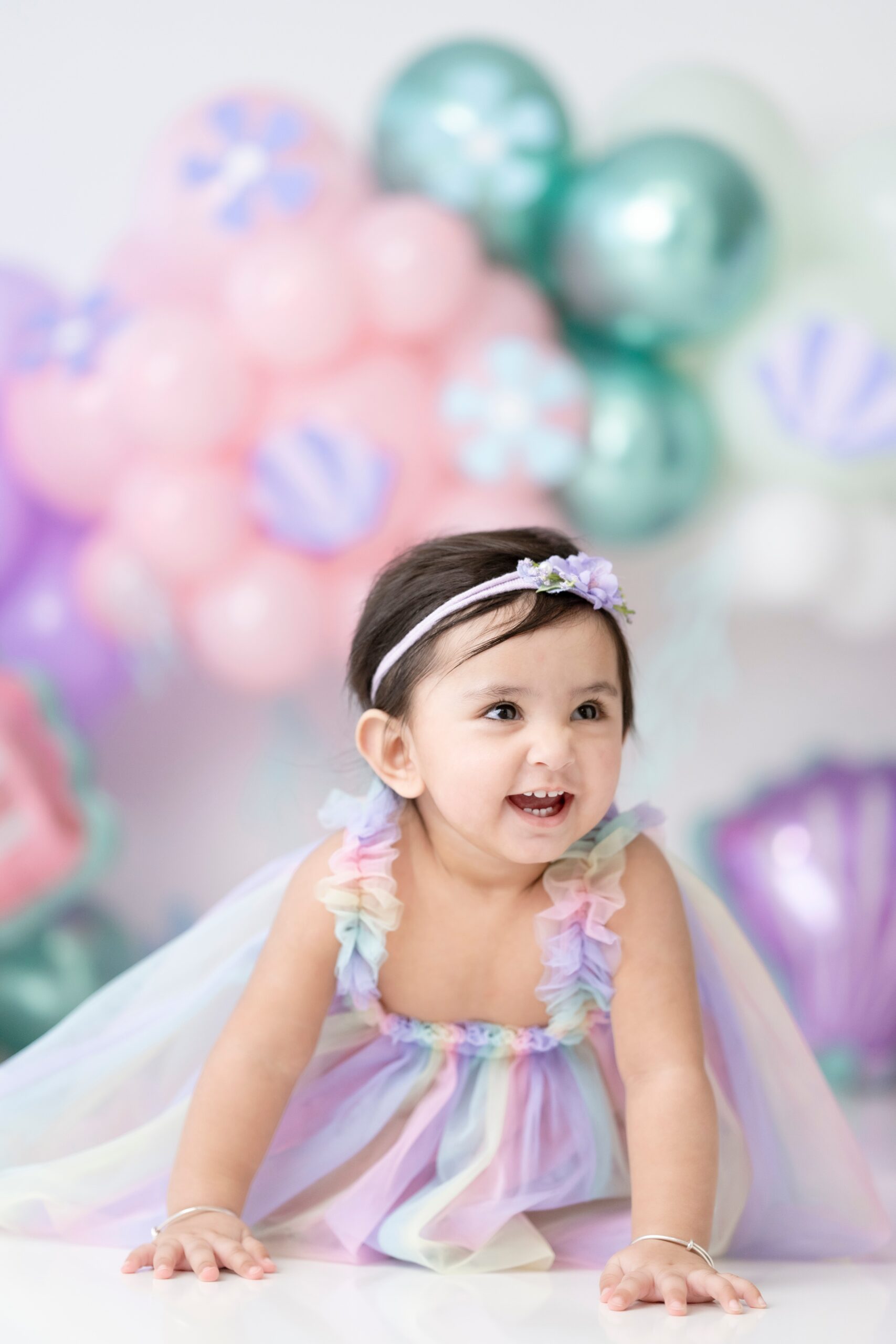 A happy toddler girl crawls on the floor of a studio in a colorful tule dress