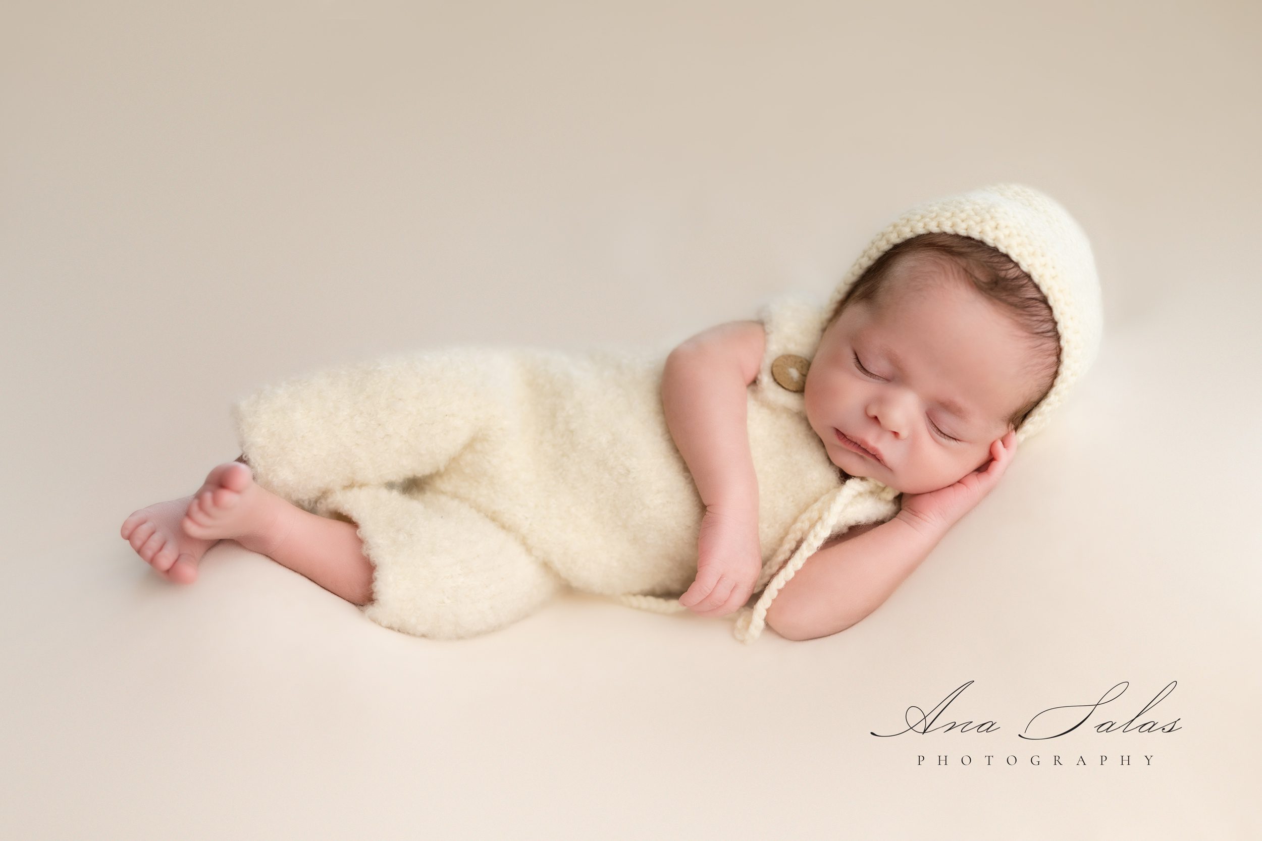 A newborn baby sleeps in a knit bonnet and matching onesie on its side after visiting baby stores in edmonton