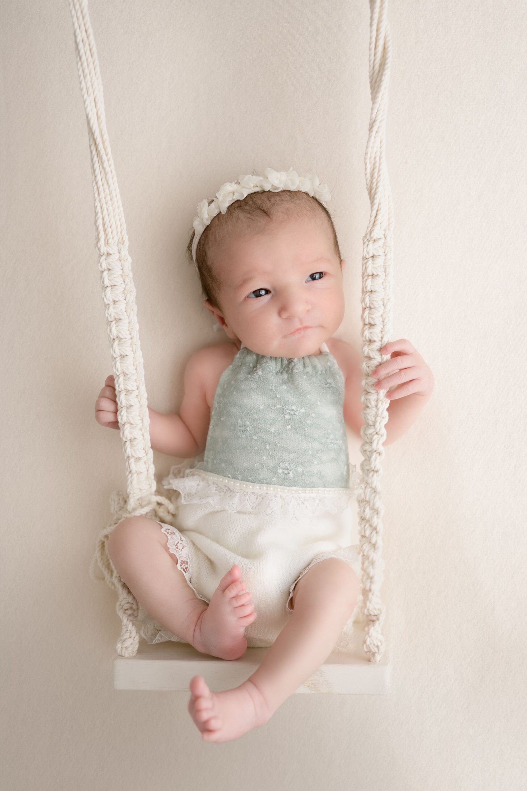 A newborn baby sits in a white swing on a bed with eyes open after visiting baby stores in edmonton