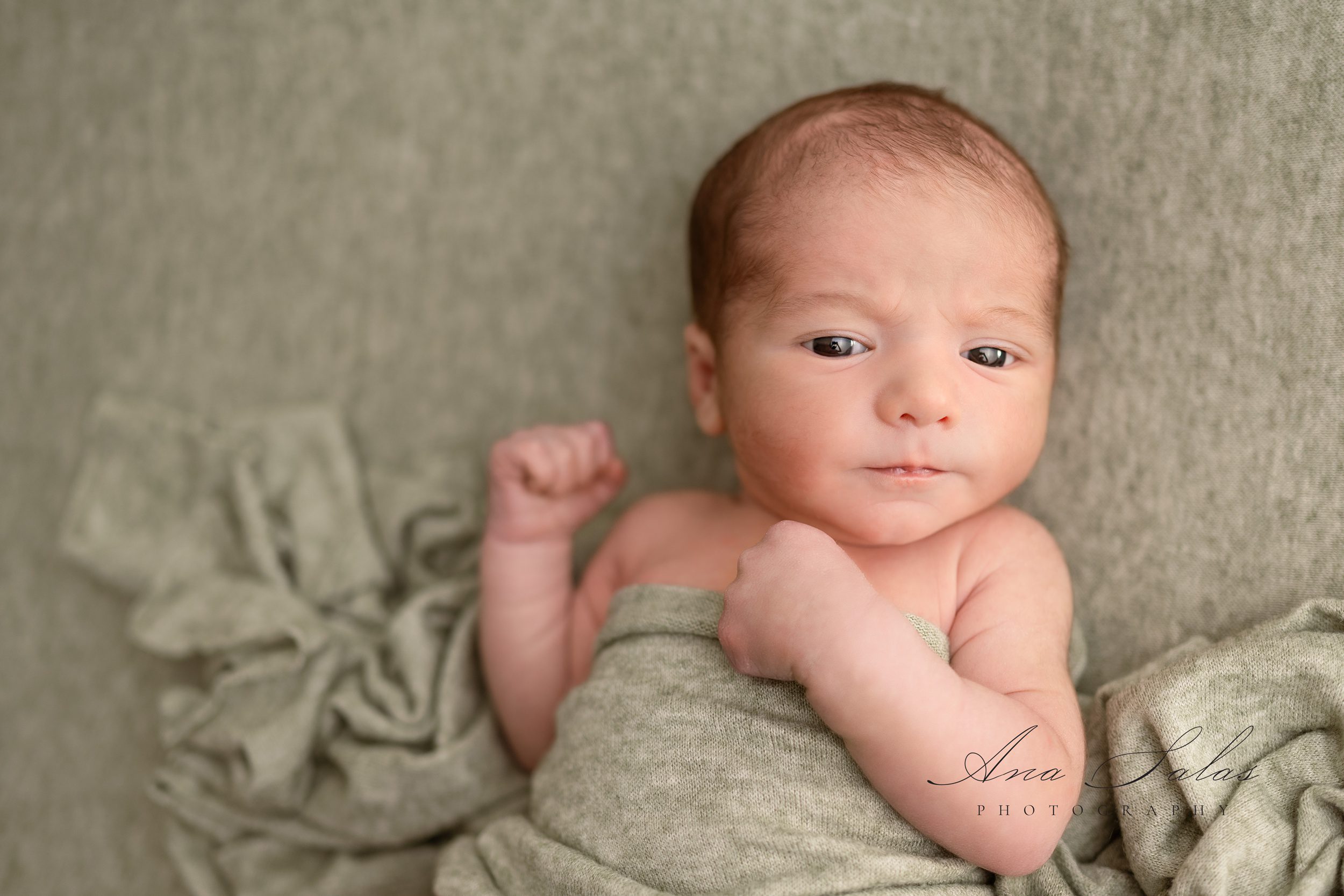 AA newborn baby lays on a grey bed under a matching blanket with eyes open after some edmonton parenting classes