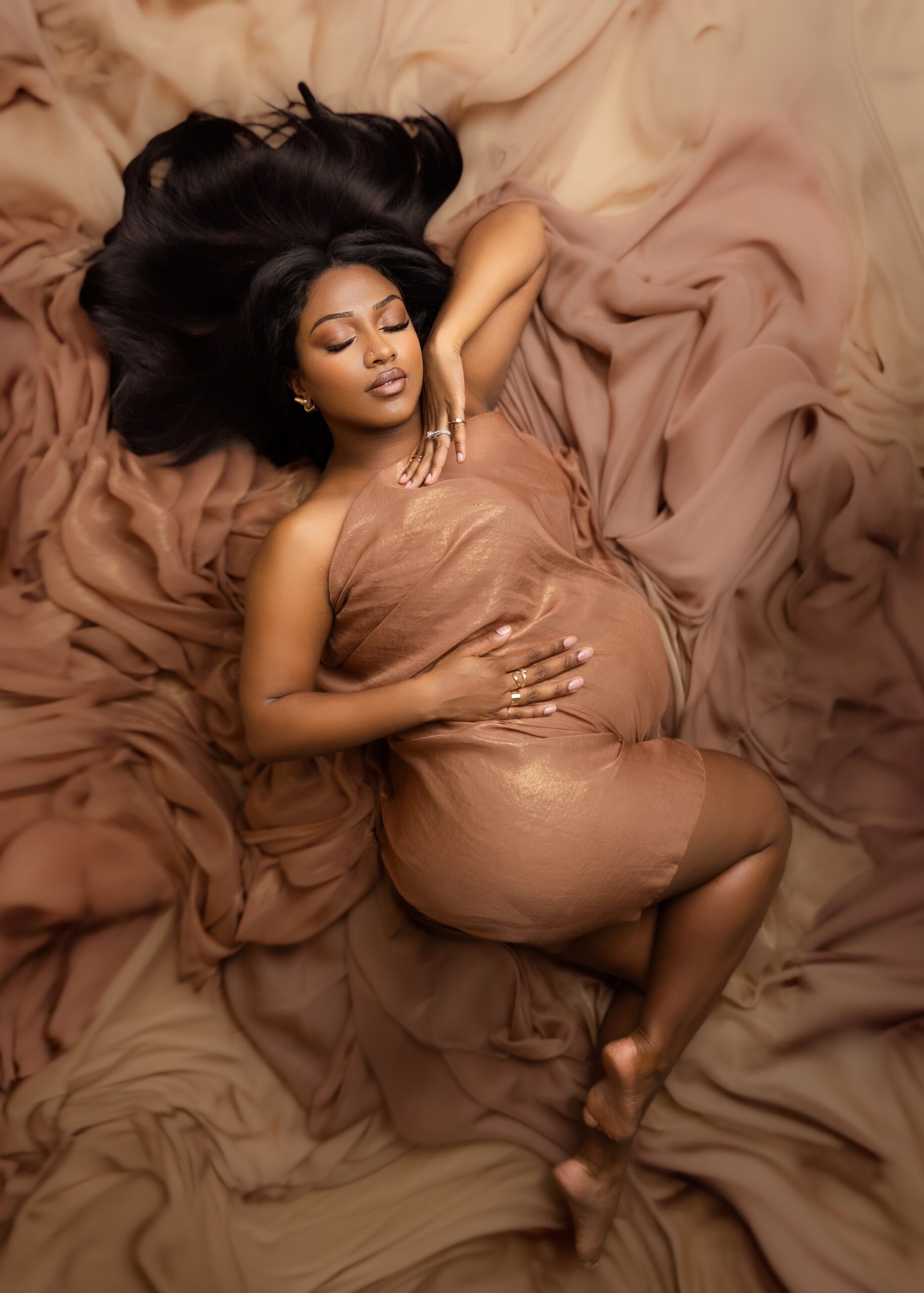 A mom to be wrapped in a brown sheet lays on a bed of flowing sheets in a studio after some pelvic floor therapy edmonton