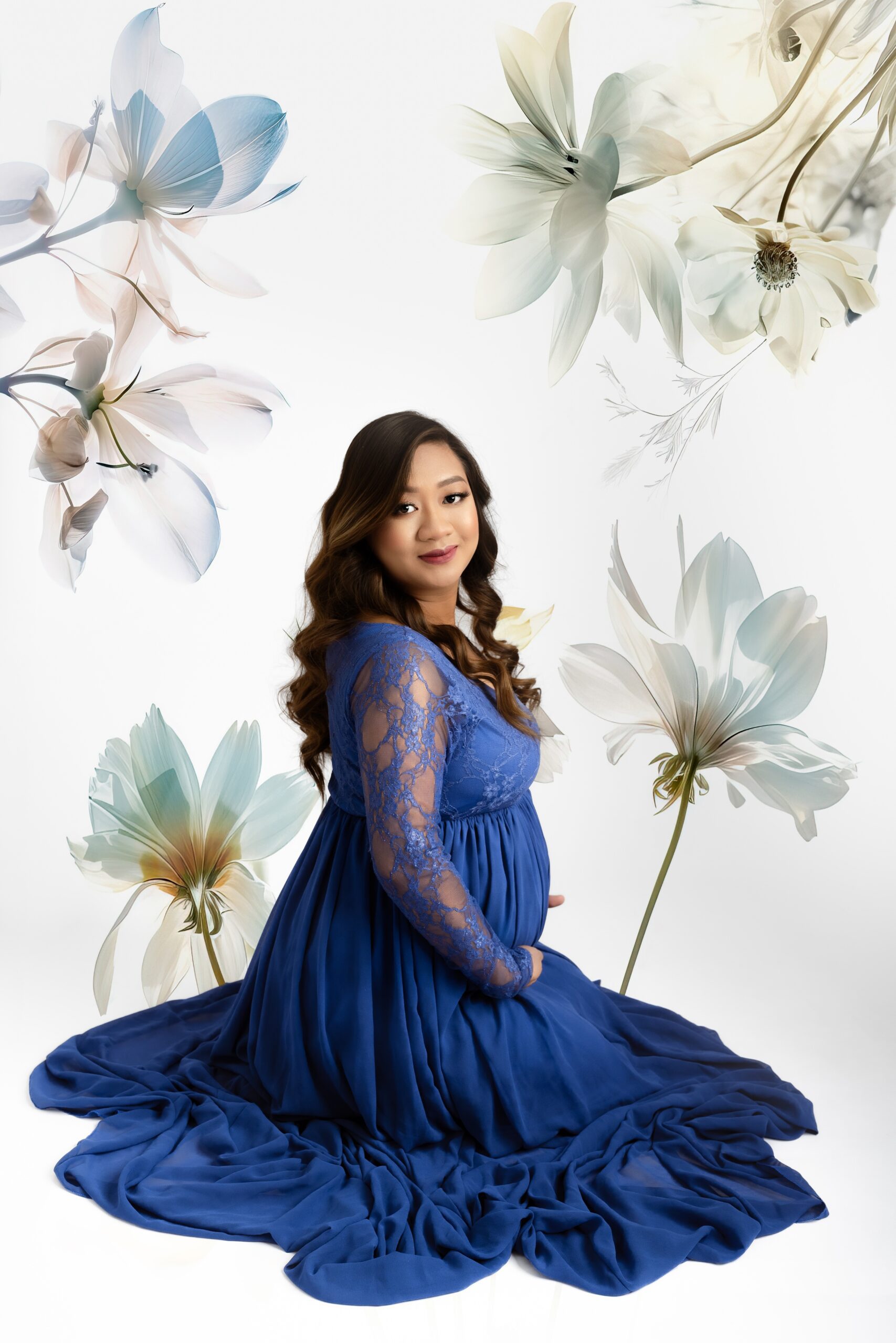 An expecting woman in a long blue maternity gown kneels on a studio floor smiling after some pregnancy acupuncture edmonton