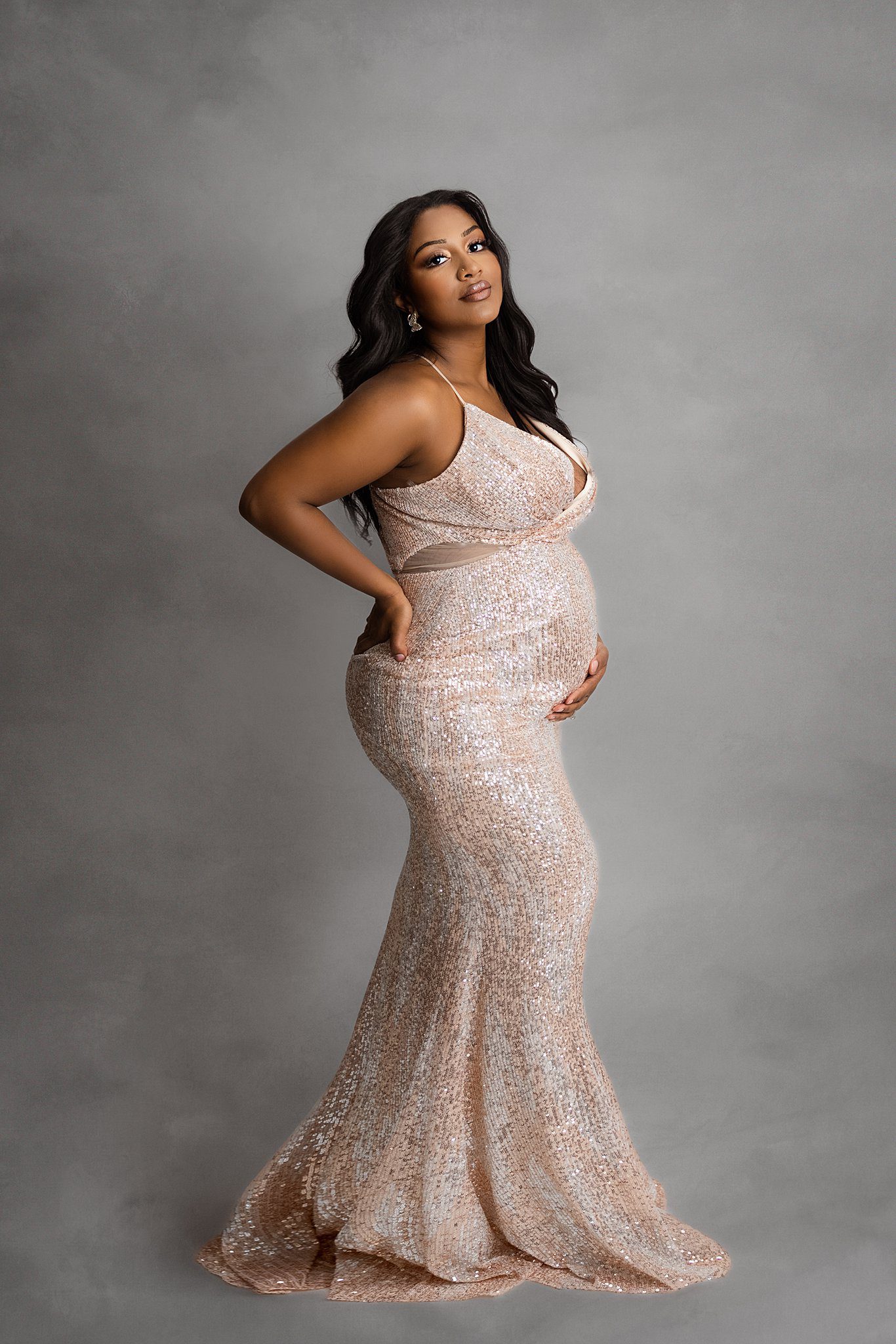 A mom to be in a glamorous maternity gown stands in a studio while holding her back and bump before her 3d ultrasound edmonton