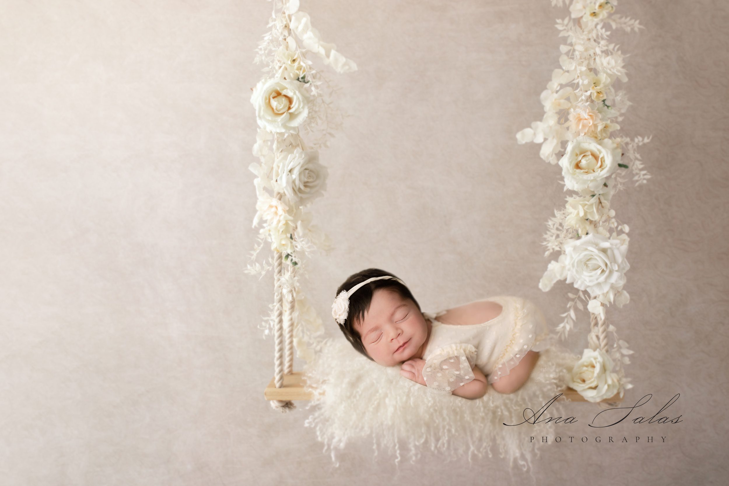 A newborn baby sleeps on a swing in a white onesie dress after meeting babysitters in edmonton