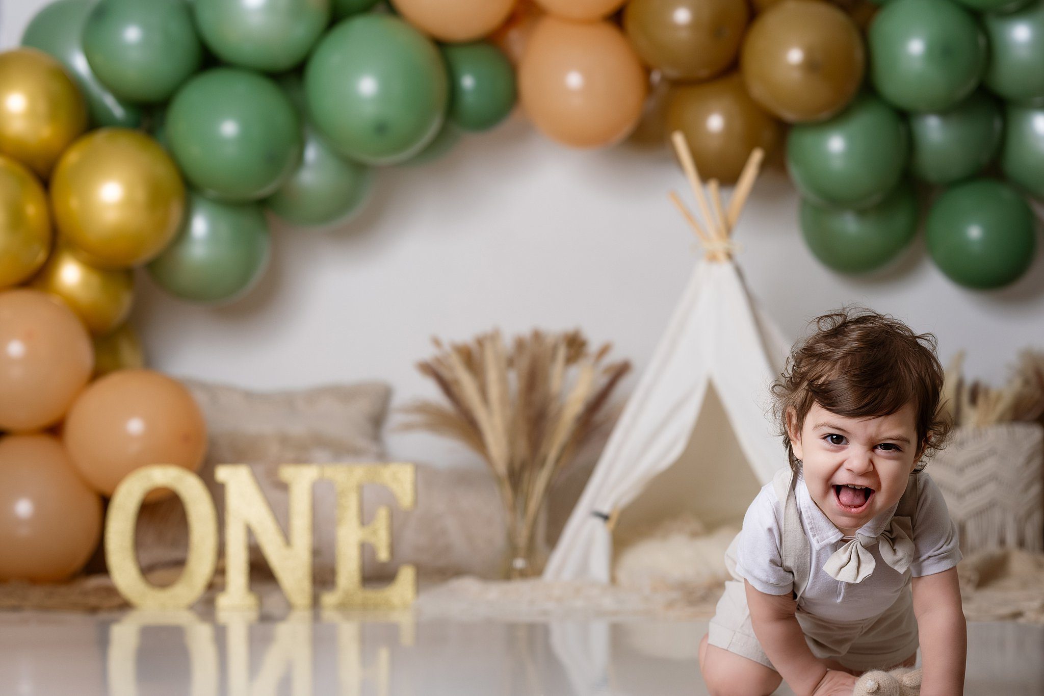 A laughing toddler crawls in a studio for his birthday with overalls and a bowtie