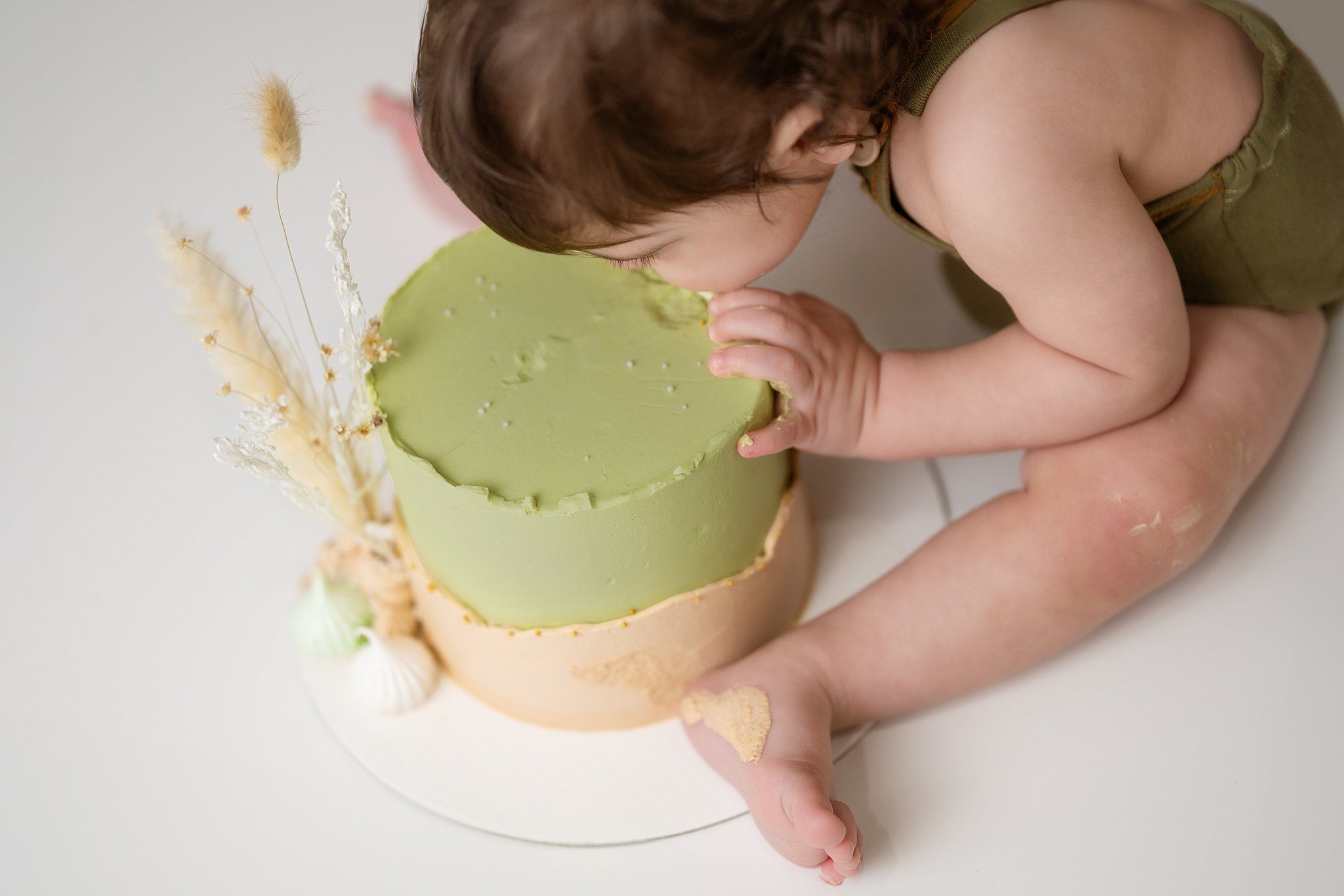 A young toddler takes a bite out of a green cake on a studio floor after visiting edmonton daycares