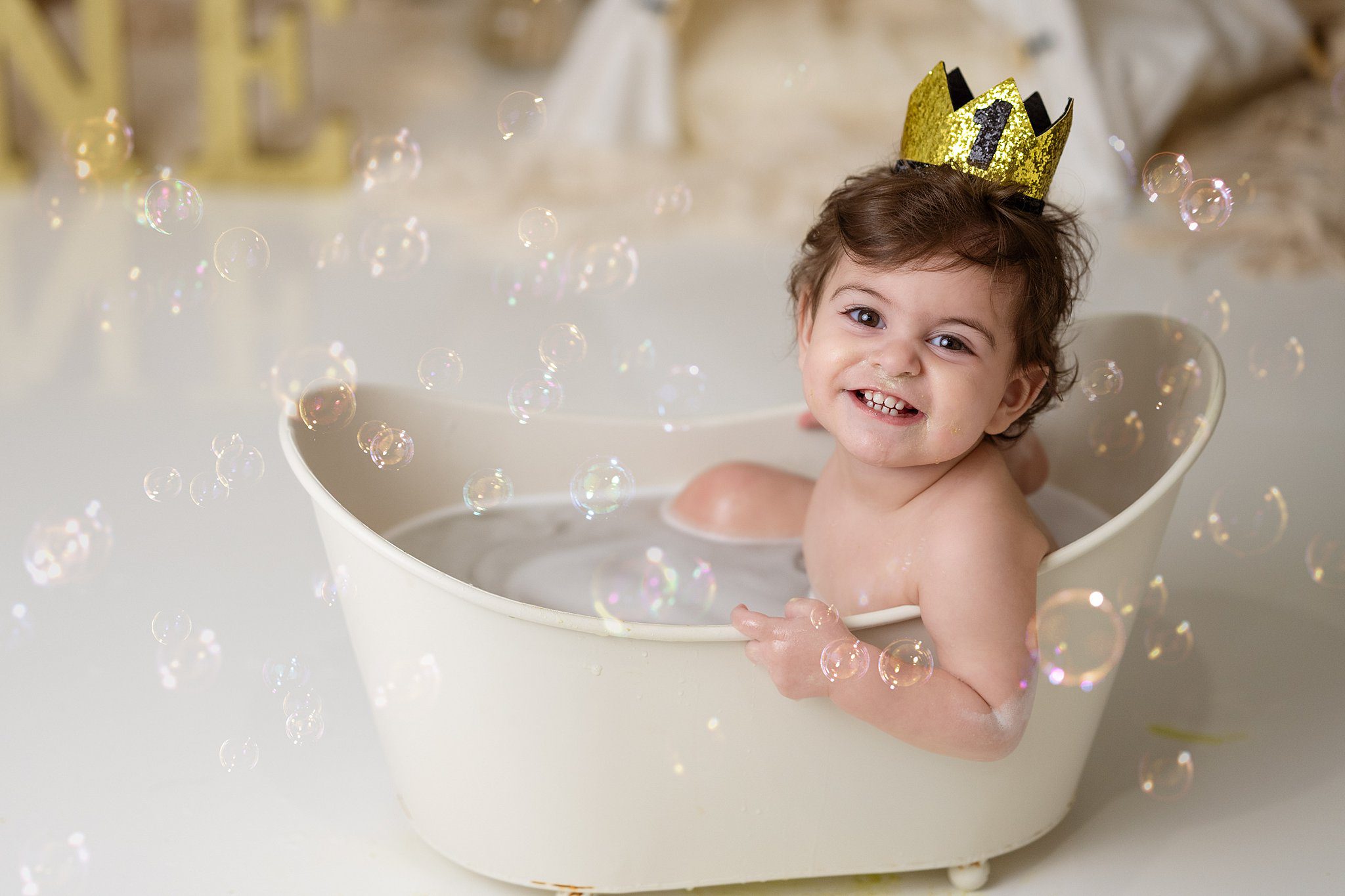 A smiling toddler sits in a tiny bathtub with a birthday crown on before visiting edmonton daycares