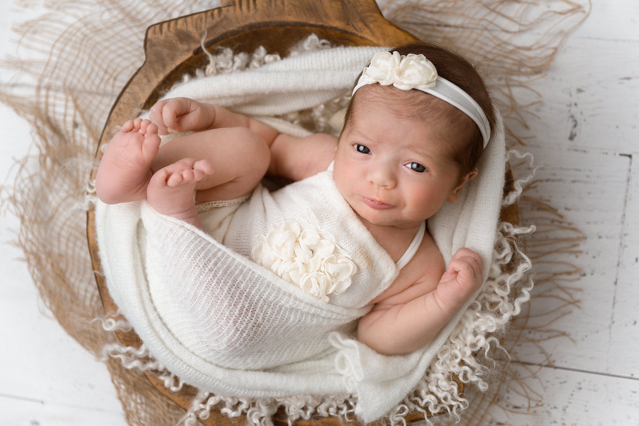 A newborn baby smirks while laying in a wooden bowl wrapped in white after meeting edmonton lactation consultant