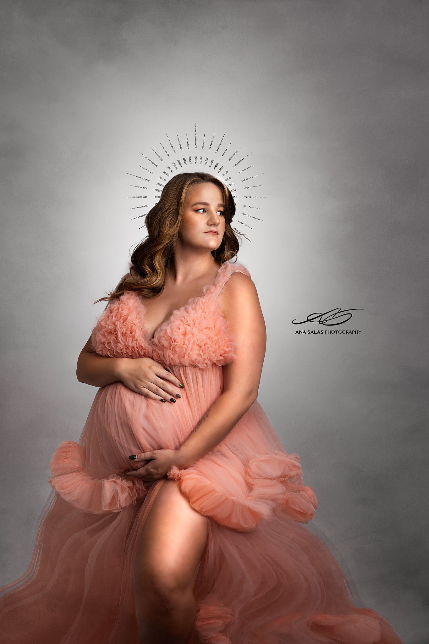 A mother to be stands in a studio in a pink tule maternity gown holding her bump after visiting lucina birth centre