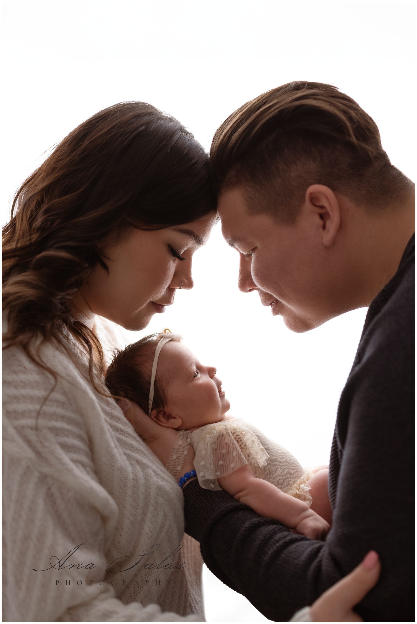 Happy new parents smile down at their newborn baby girl in dad's hands in a studio