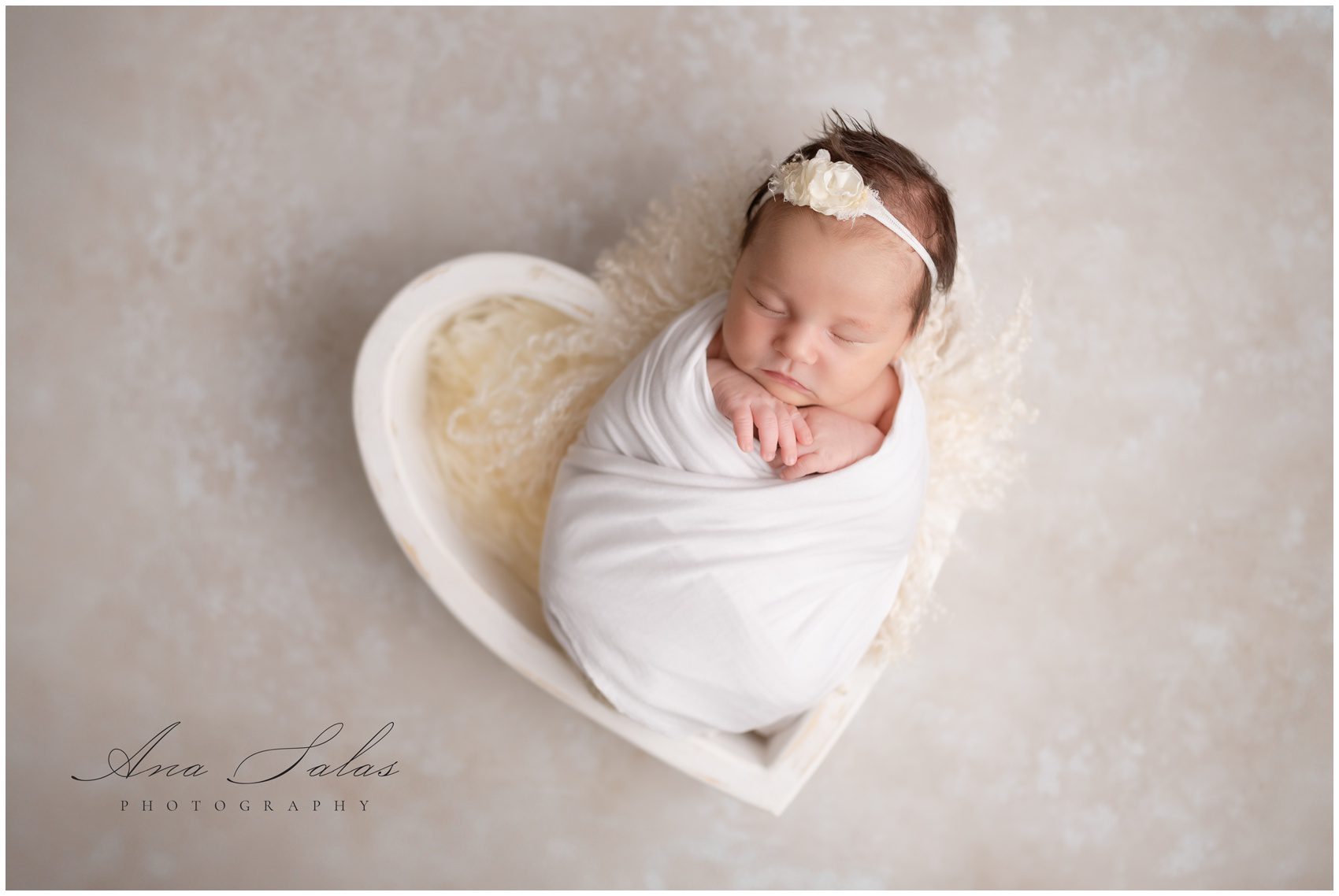 A sleeping newborn baby girl in a white egg swaddle in a wooden heart shaped bowl after meeting an edmonton postpartum doula