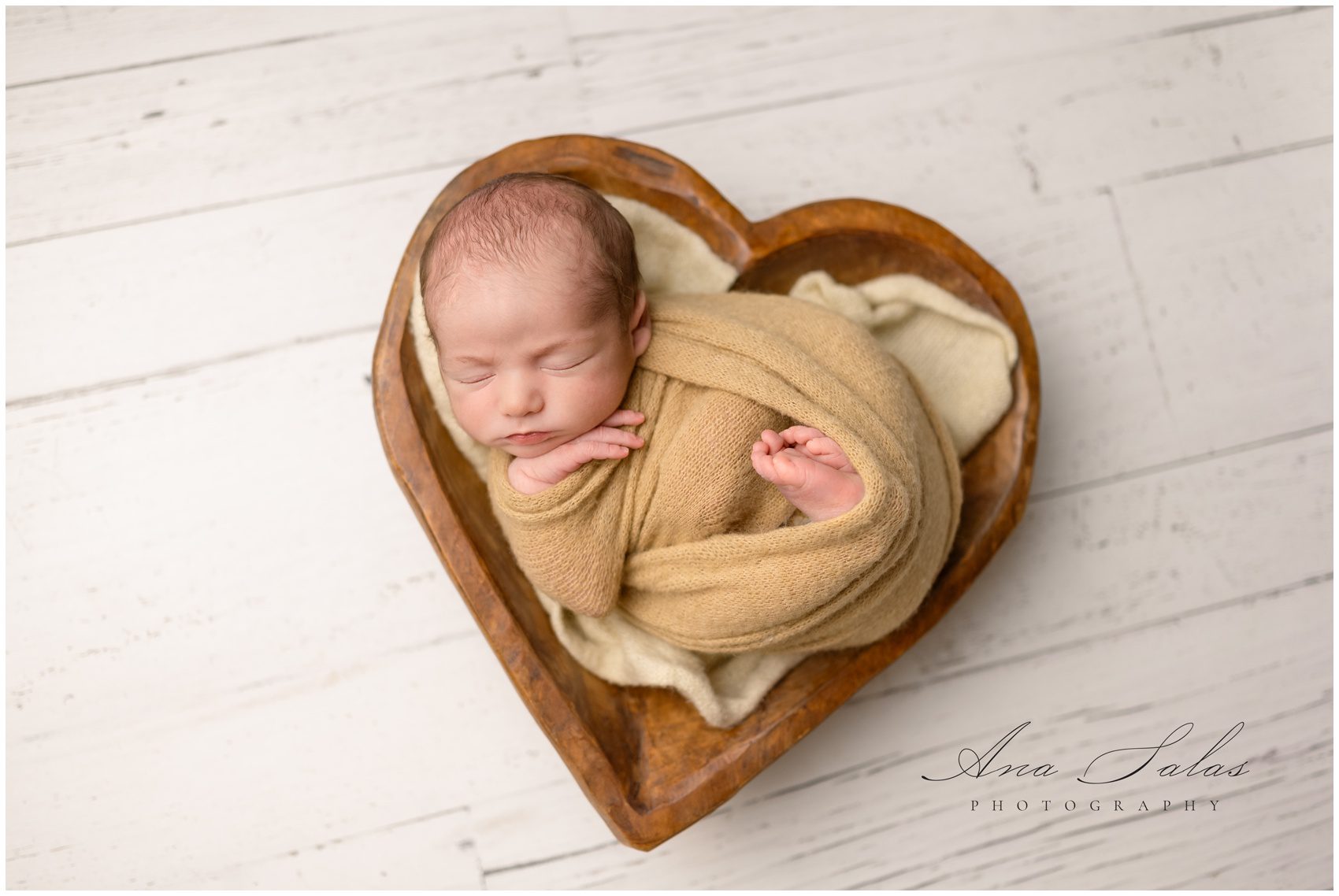 A newborn baby sleeps in a wooden bowl while wrapped up in a brown swaddle after meeting an edmonton postpartum doula