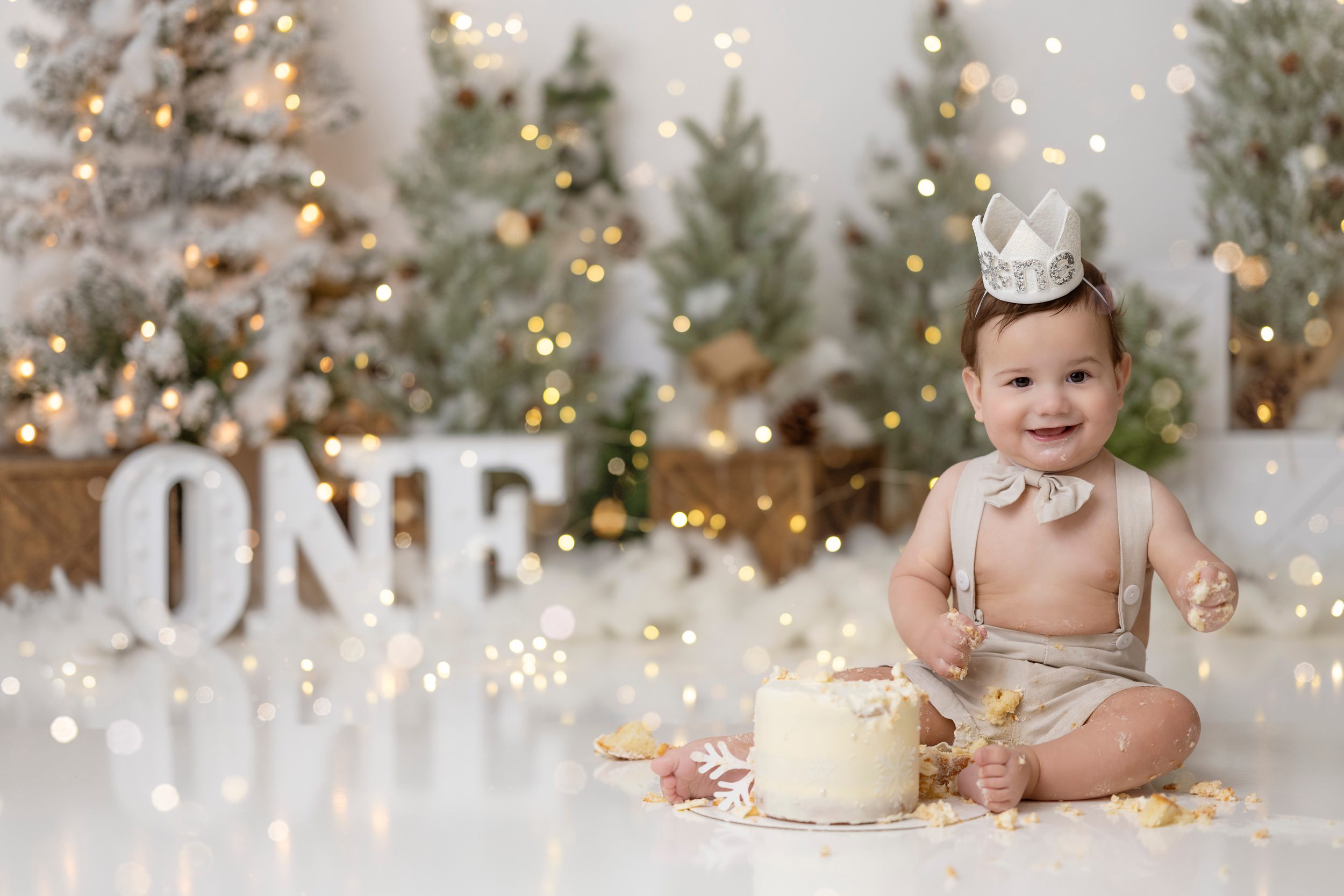 A happy toddler boy sits in a christmas themed studio for his first birthday