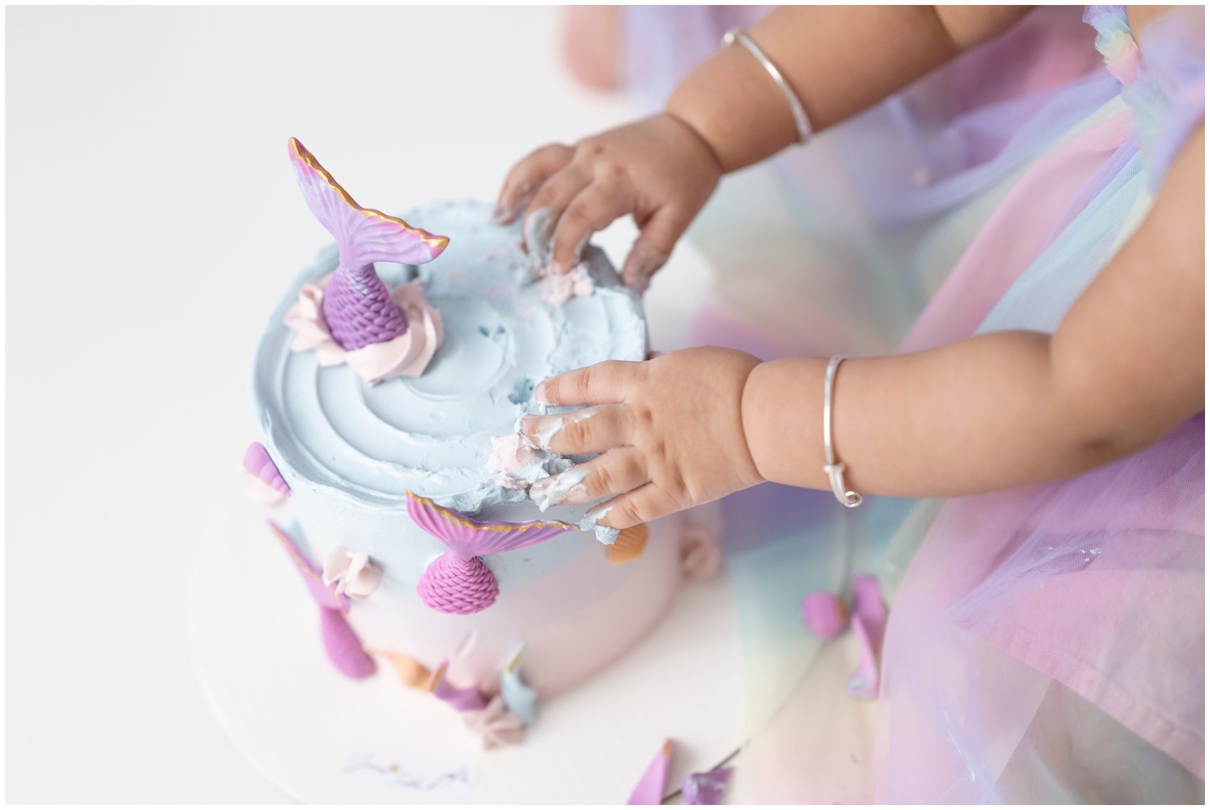 Details of a toddler girl playing in her mermaid themed cake in a colorful dress before visiting indoor playgrounds edmonton