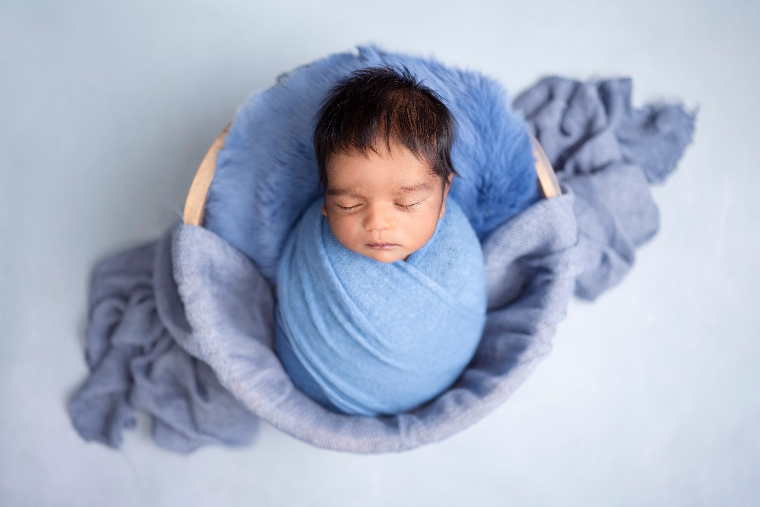 A newborn baby wrapped tight in blue swaddle in a wooden basket before some infant swim lessons edmonton