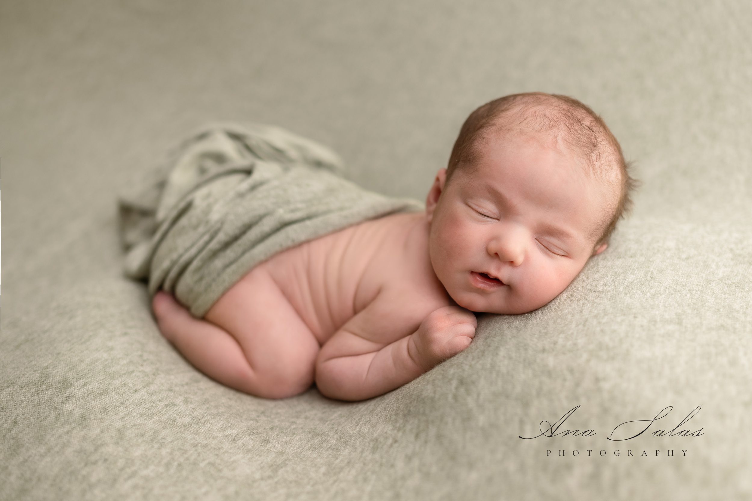 A newborn baby sleeps in froggy pose on a pad under a blanket before some infant swim lessons edmonton