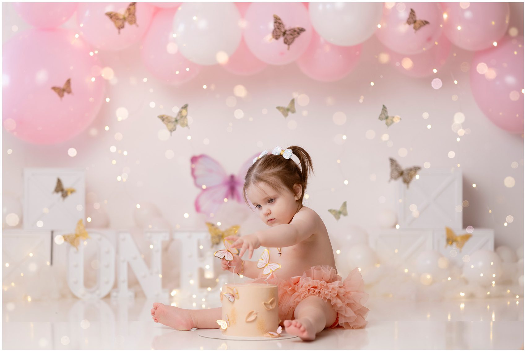 A toddler girl sits in a studio playing with her butterfly themed birthday cake after exploring montessori schools in edmonton