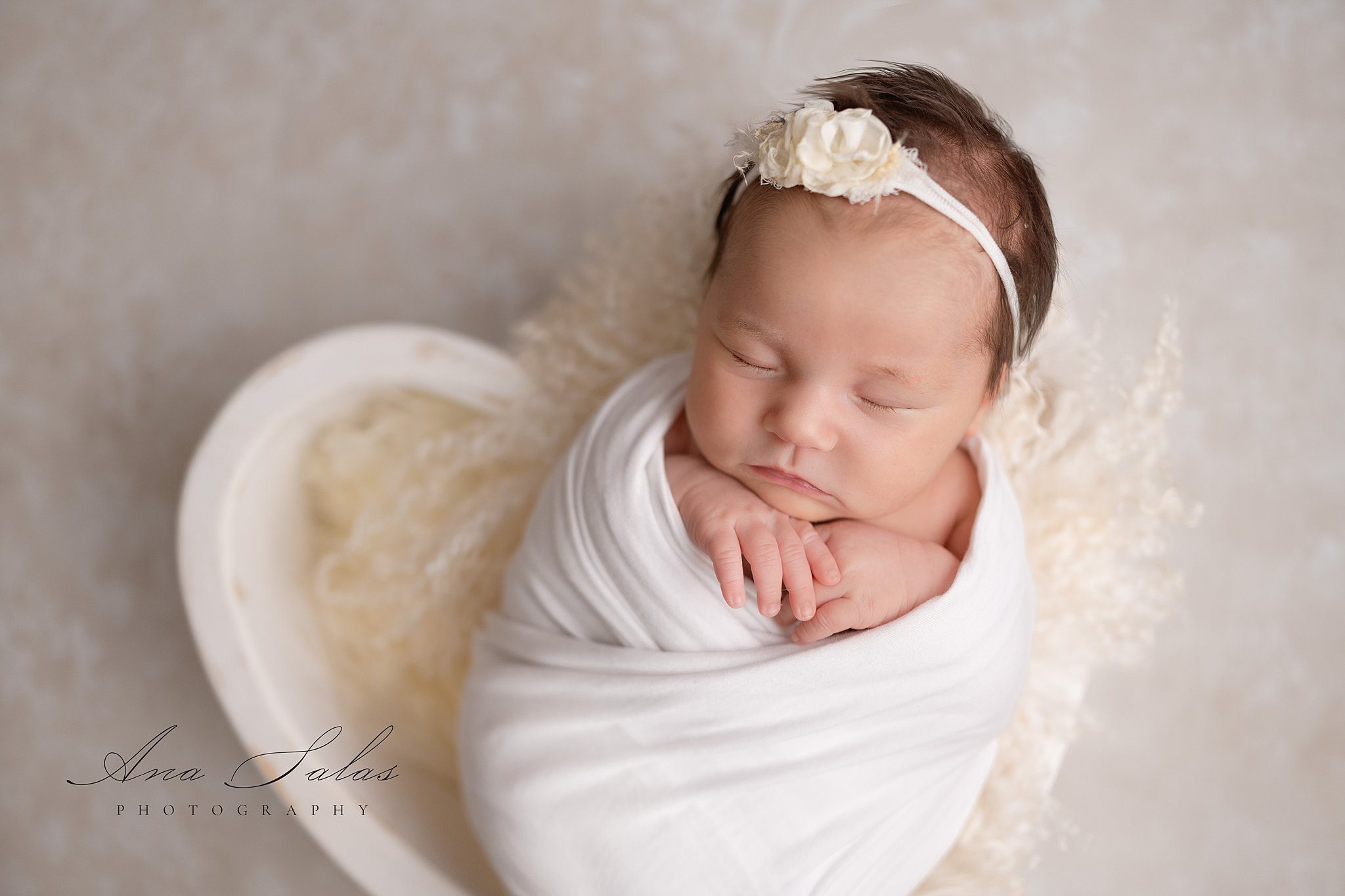 A newborn baby sleeps in a white swaddle with hands out and a floral headband after meeting mommy connections edmonton