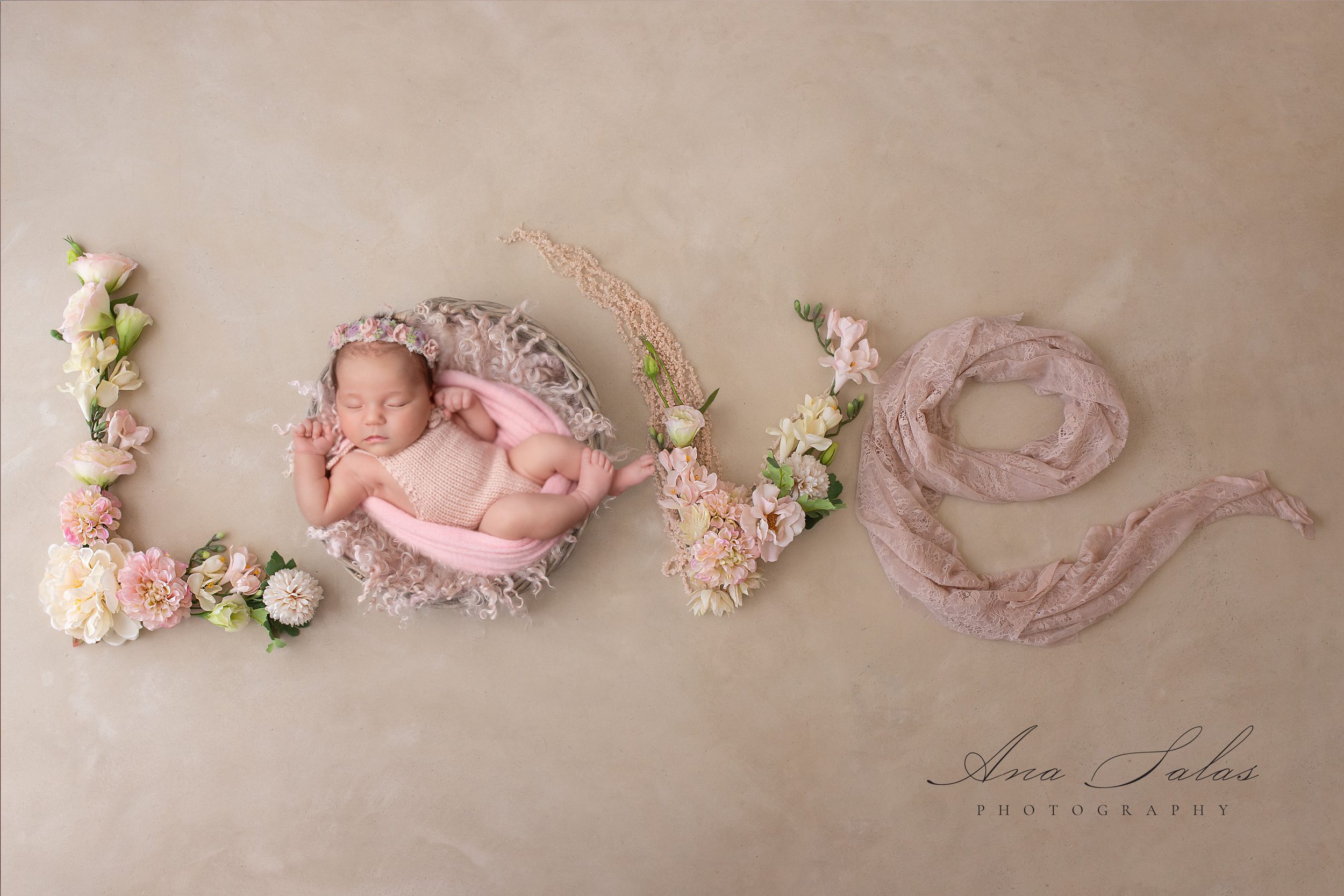 A newborn baby sleeps in a wicker bowl as flowers and fabric spell LOVE around her after visiting tiny hoppers edmonton