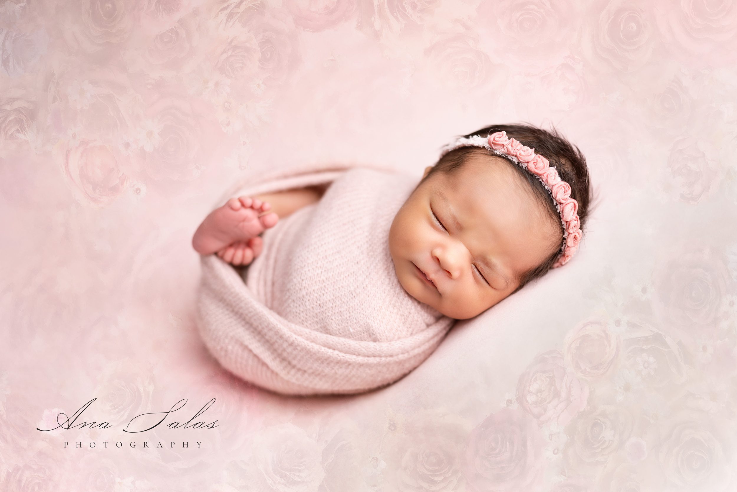 A baby girl sleeps in a flower headband and matching pink swaddle