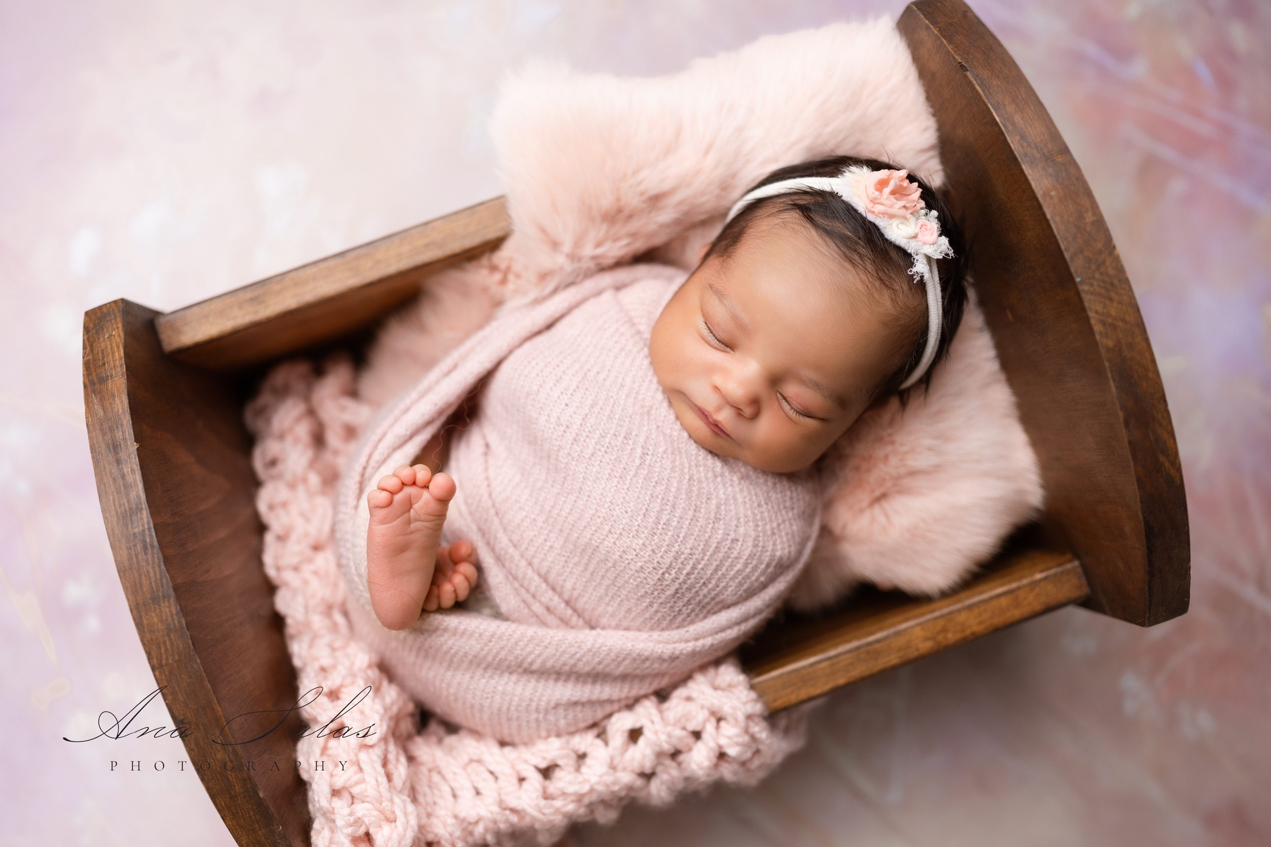 A sleeping newborn baby in a small wooden crib wrapped in a tight pink swaddle after meeting mini dreamers edmonton