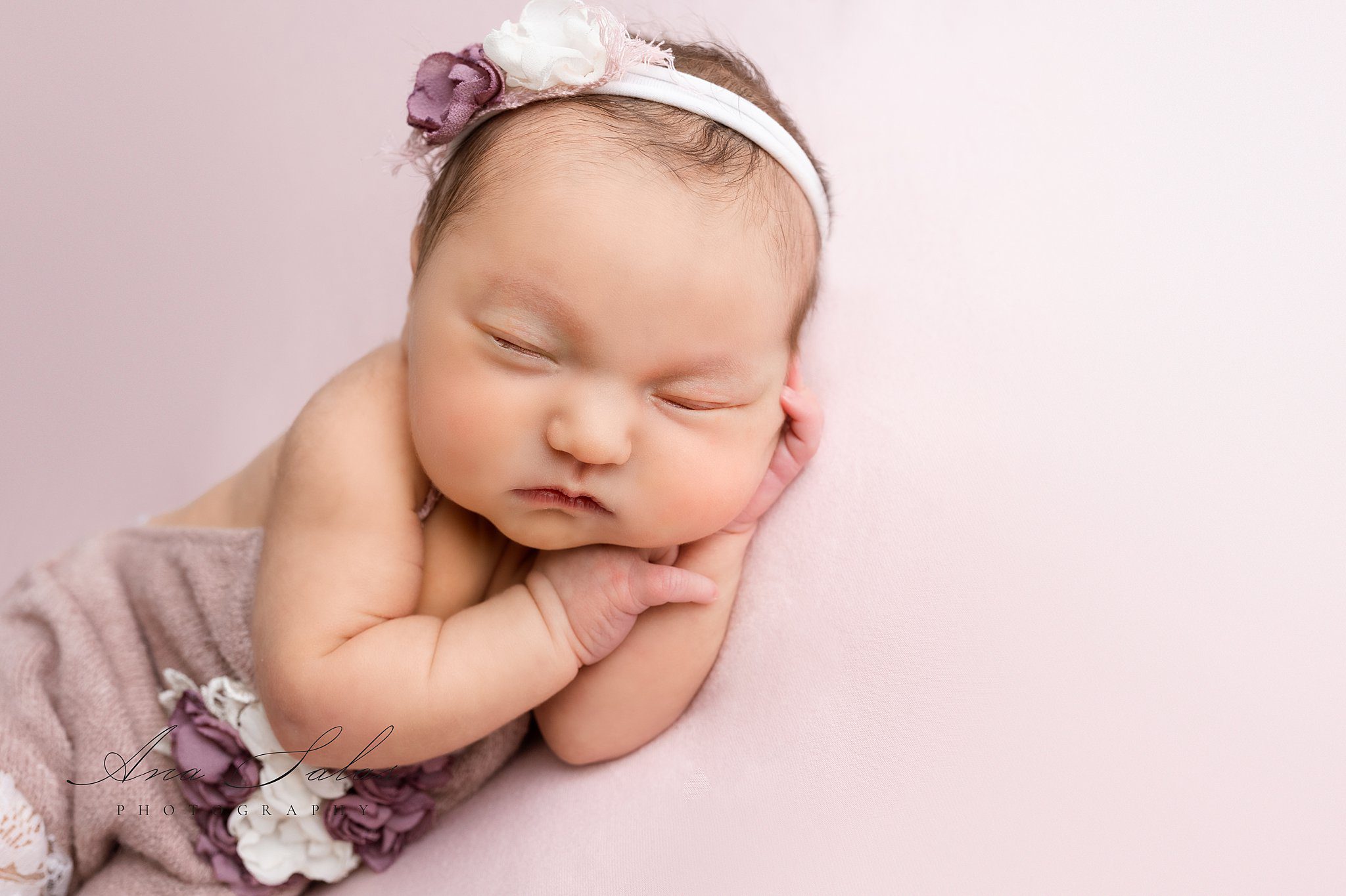 A sleeping newborn baby girl on her side in a pink onesie