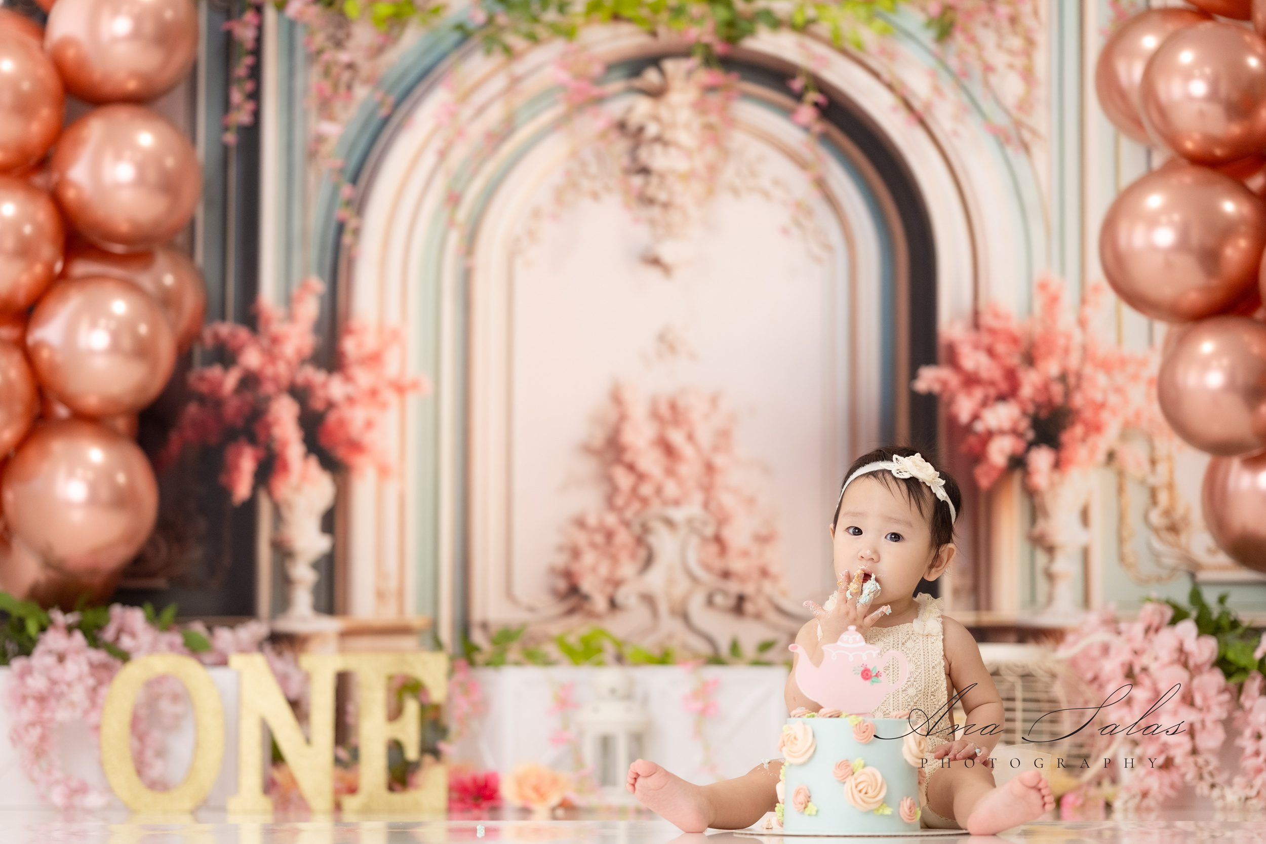 A baby sits on the floor of a studio eating a cake between her legs after visiting princess and the pea boutique