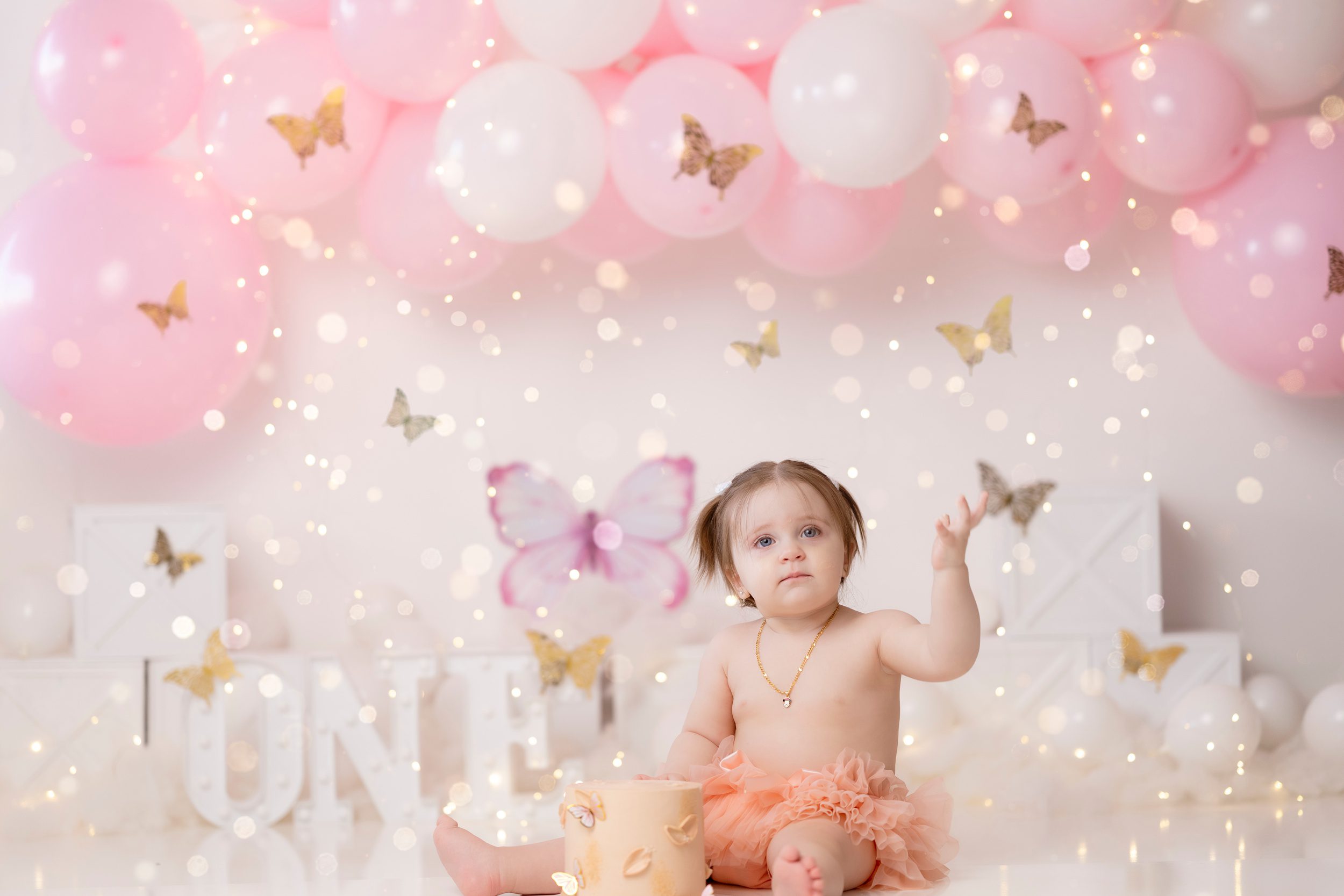 a baby girl in a pink tutu sits in a studio with her birthday cake surrounded by bubbles