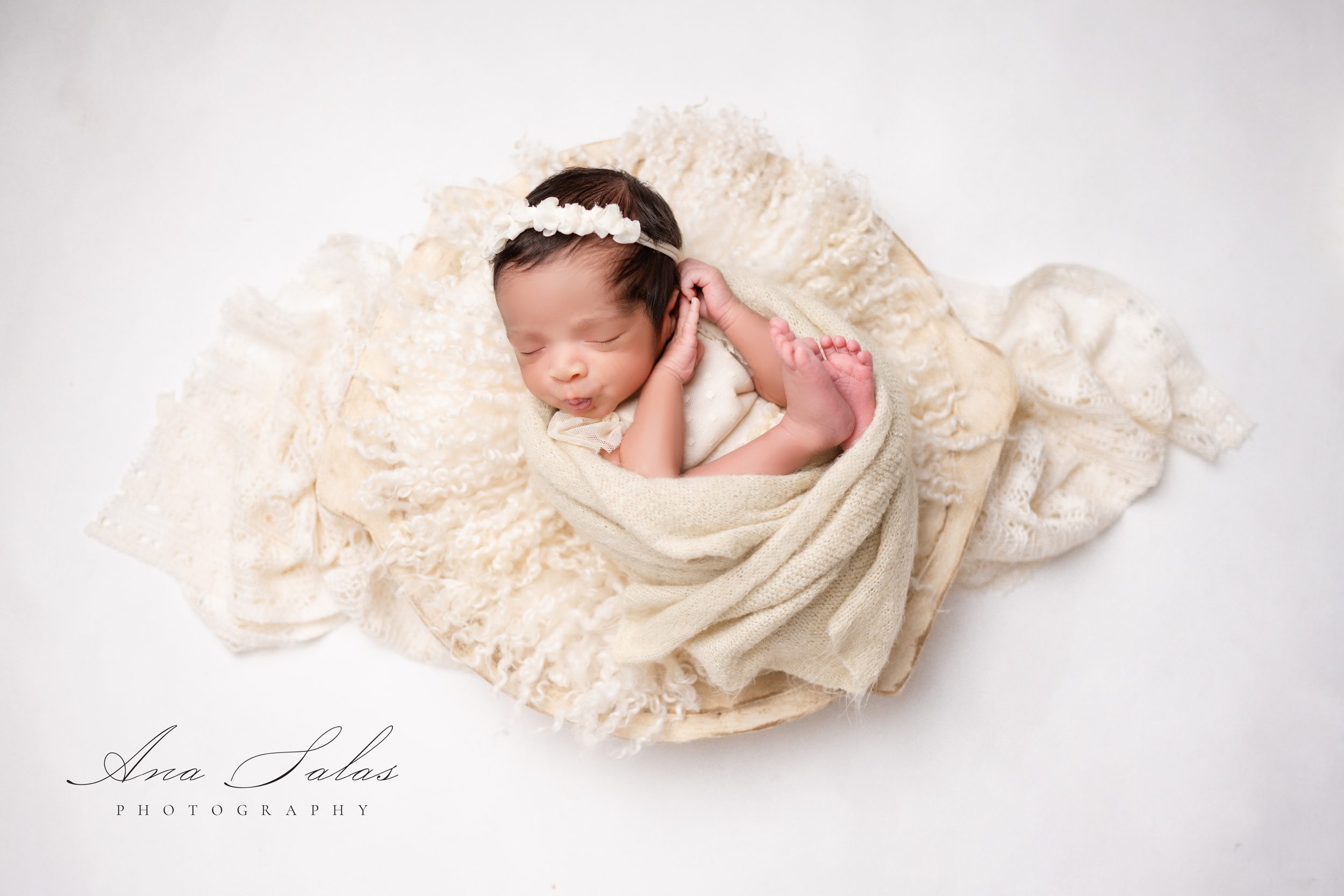 A sleeping newborn baby girl wrapped in a blanket in a dress in a studio