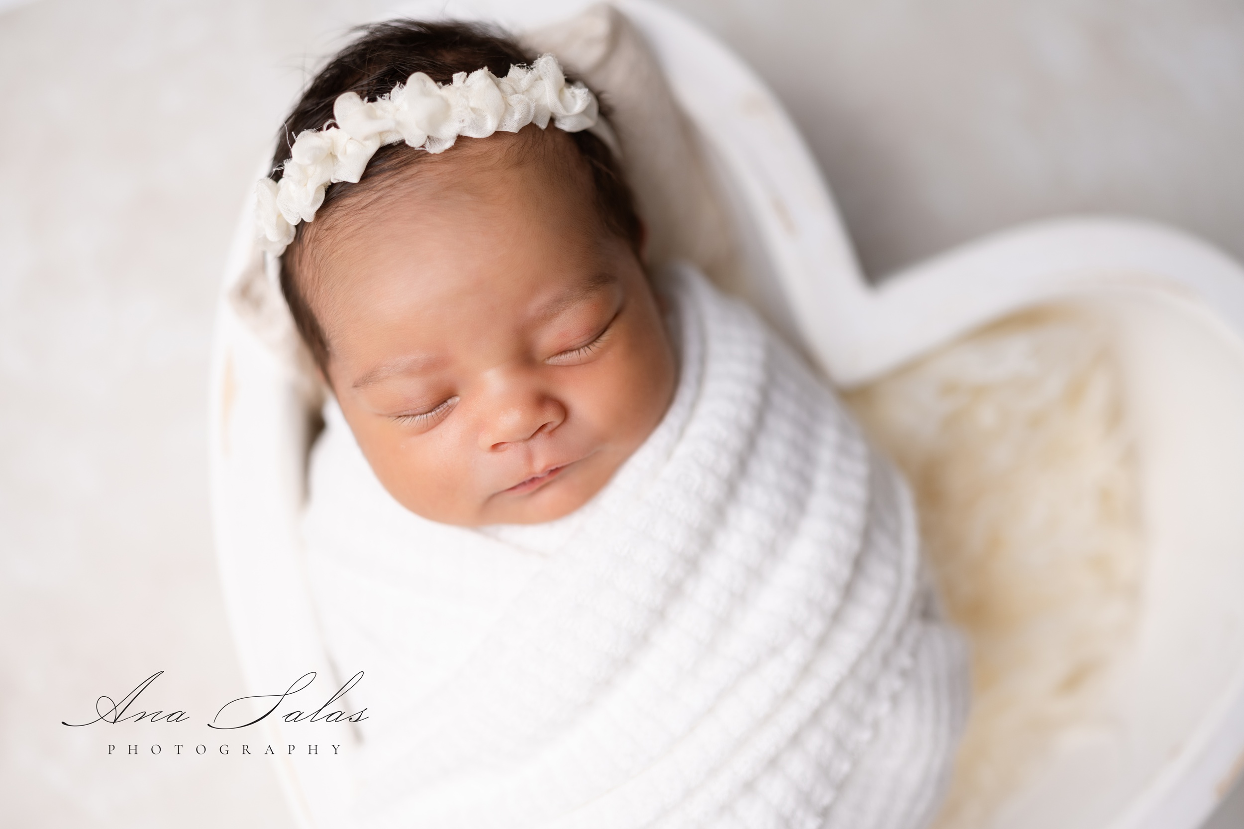 Close up of a newborn girl in a headband sleeping in a white heart bowl