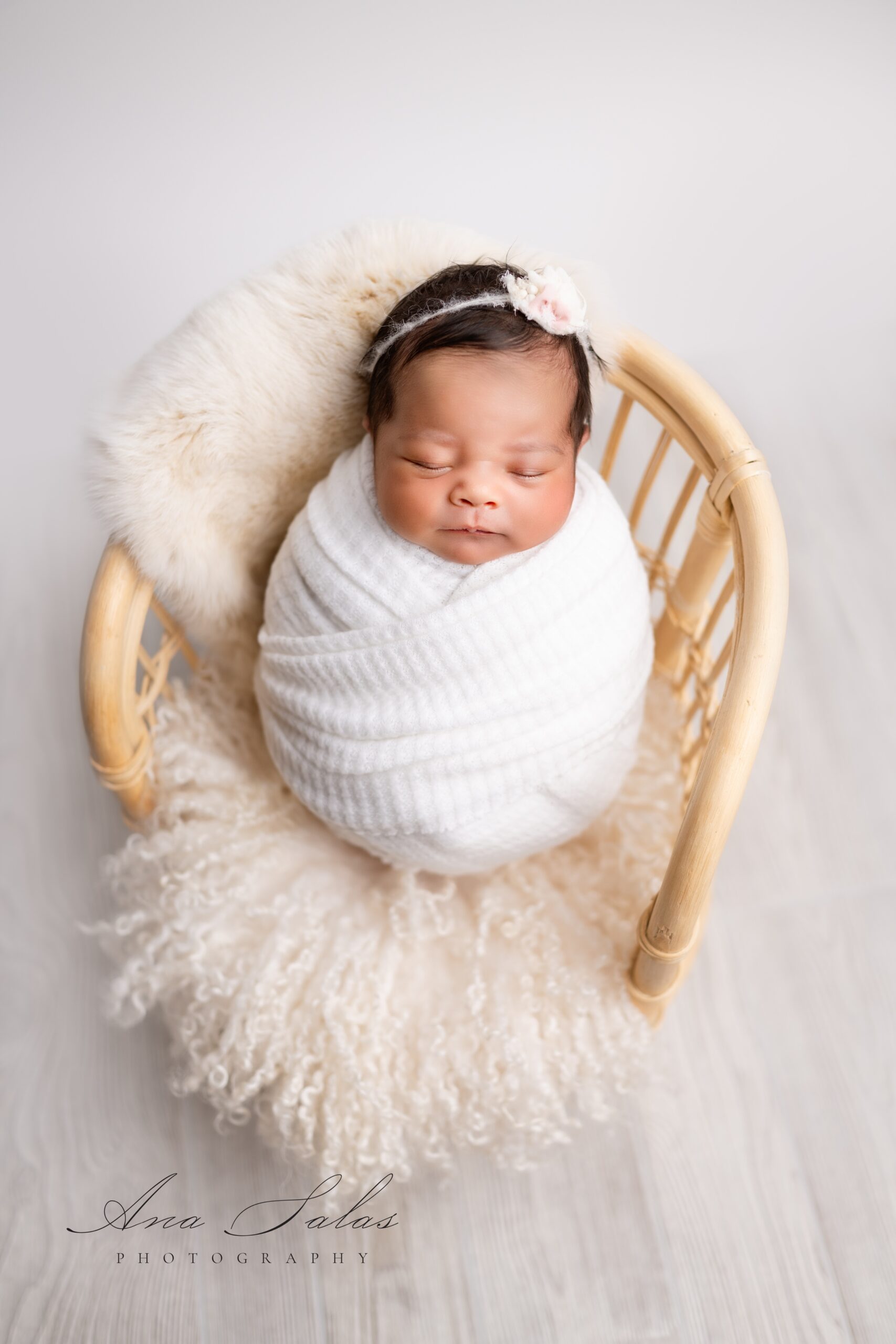 A newborn baby girl in a tight white swaddle sleeps in a tiny wicker chair after meeting nourish lactation