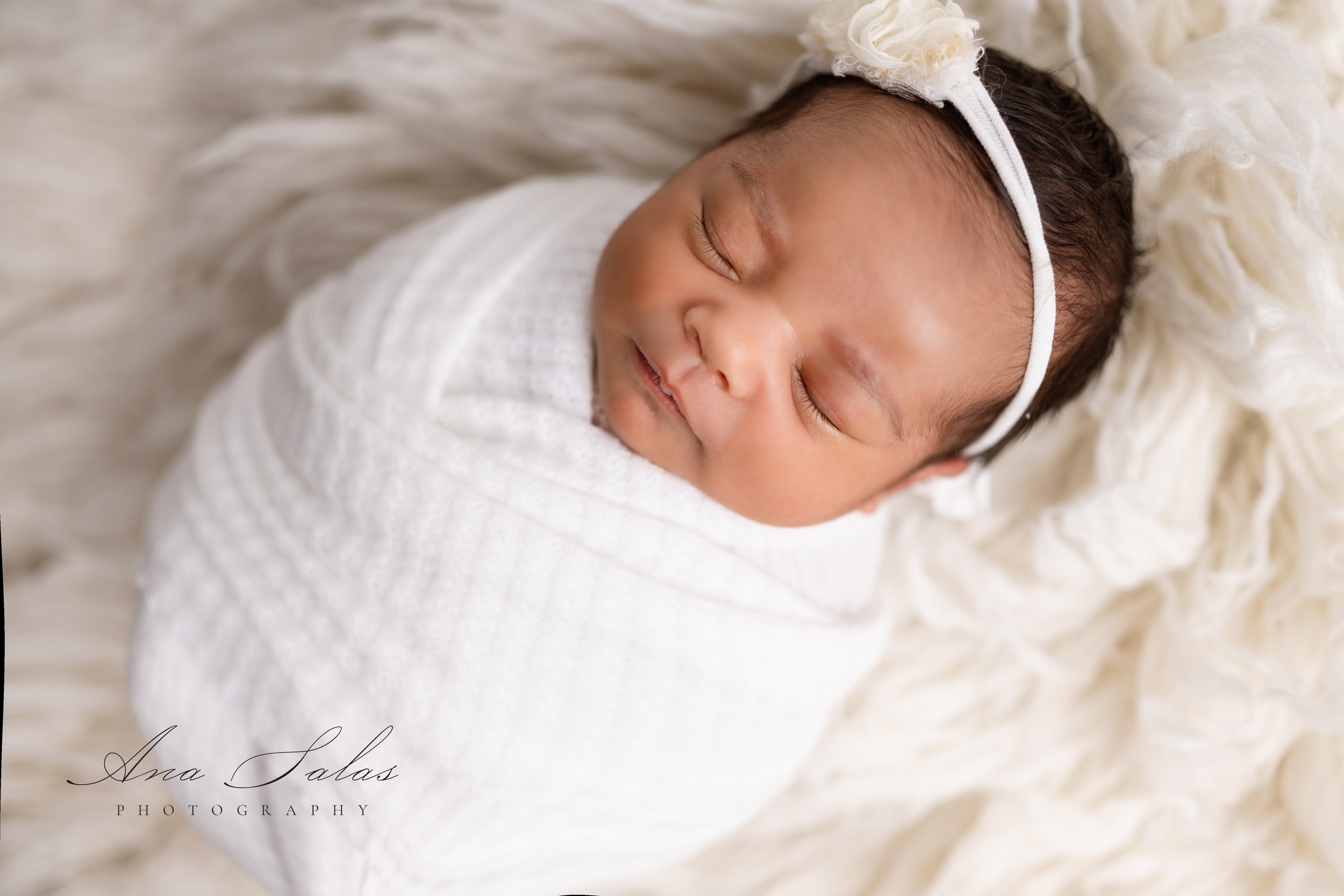 A newborn baby girl sleeps in a white onesie and headband thanks to nourish lactation